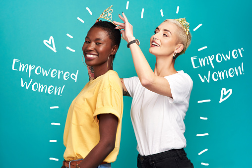 Studio shot of a young woman putting a crown on her friend against a turquoise background