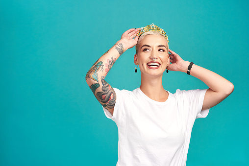Studio shot of a young woman putting a crown her head against a turquoise background