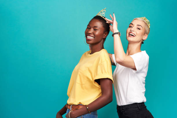 Who runs the world? We do! Studio shot of a young woman putting a crown on her friend against a turquoise background womens issues stock pictures, royalty-free photos & images