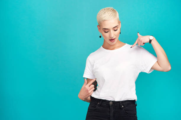 Just waiting for your words... Studio shot of a confident young woman pointing at her t shirt against a turquoise background blank t shirt stock pictures, royalty-free photos & images