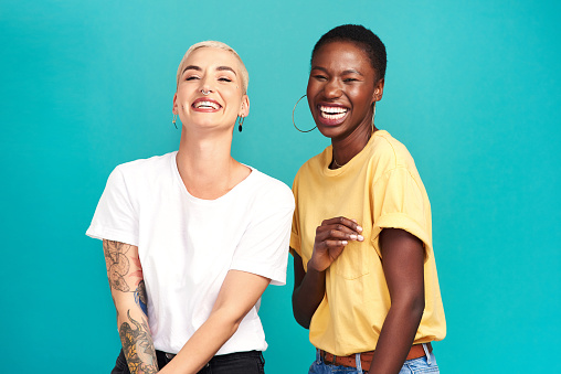 Studio shot of two happy young women posing together against a turquoise background