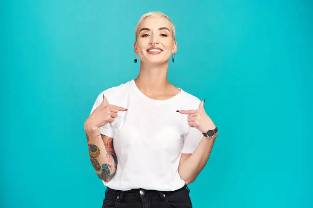 Studio shot of a confident young woman pointing at her t shirt against a turquoise background