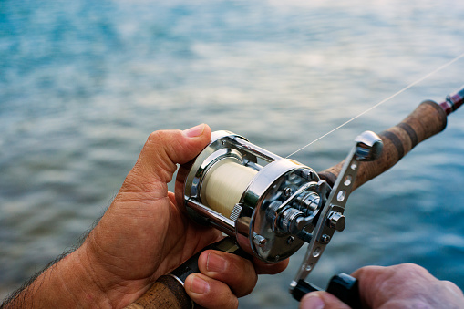 A close-up of a fisherman holding a fishing rod and winding a fishing reel.