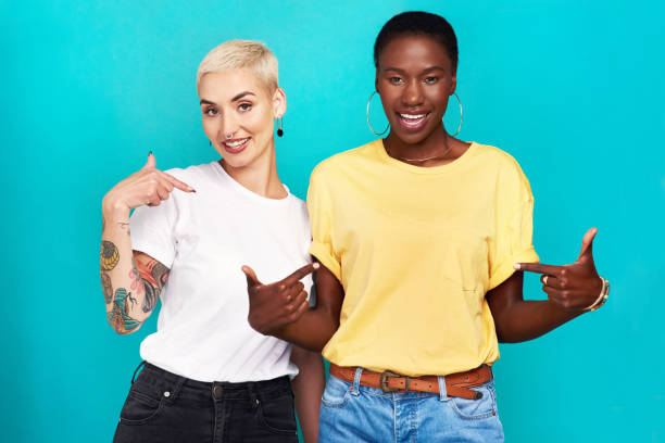 Speak your truth Studio shot of two confident young women pointing at their t shirts against a turquoise background LGBTQ -Owned Brands stock pictures, royalty-free photos & images