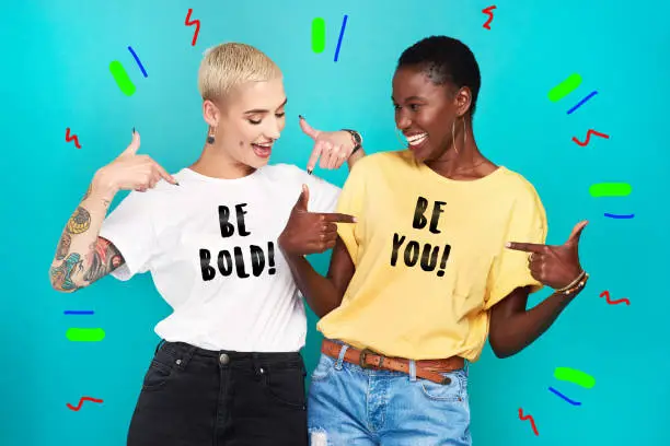 Studio shot of two confident young women pointing at their statement t shirts against a turquoise background