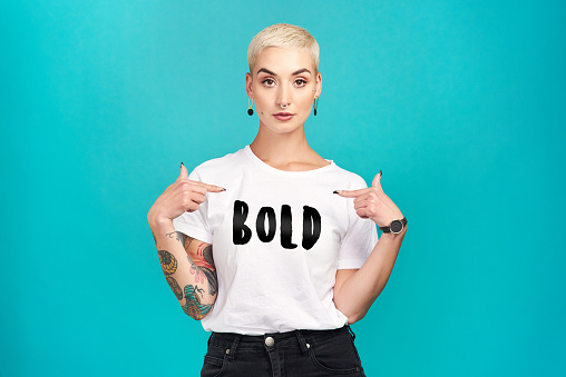 Studio shot of a confident young woman wearing a t shirt with “bold” on it against a turquoise background