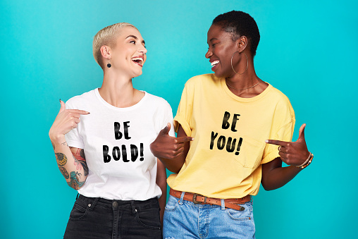 Studio shot of two confident young women pointing at their statement t shirts against a turquoise background