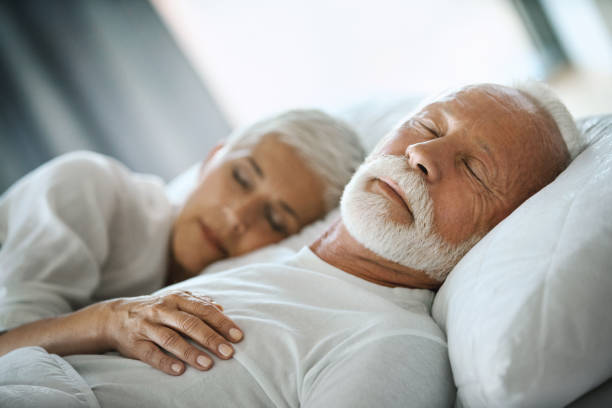 Mature couple sleeping. Closeup of mid 60's couple sleeping late in the morning in an already brightly lit bedroom. body positive couple stock pictures, royalty-free photos & images