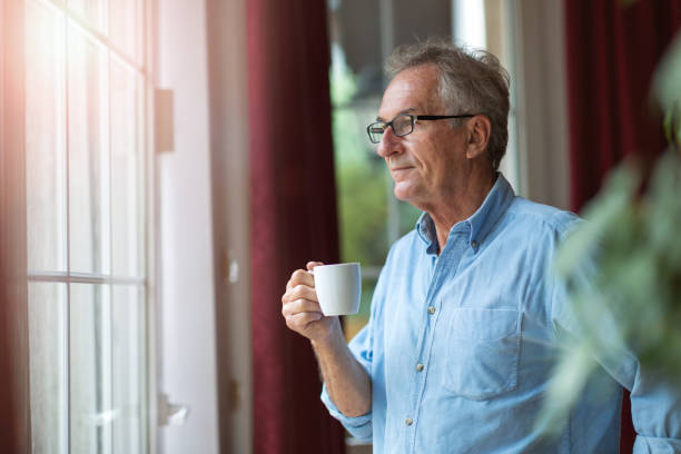 istock Relaxed mature man at home standing by the window 1170307680