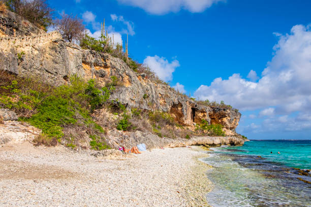 Tourists enjoying the pebble beach and the clear, turquoise waters at the 1000 Steps dive site and beach, one of the great spots for diving and snorkeling in Bonaire, in the Caribbean Netherlands.