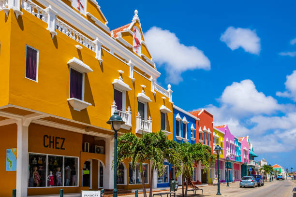 The pink Dutch style Royal Plaza with two palm trees at the side. It is set off with white clouds and blue sky. This building is an icon for Oranjestad.