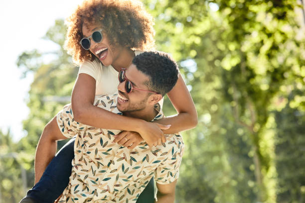 Cheerful young couple enjoying piggyback ride Cheerful young couple enjoying piggyback ride in city. Playful man and woman spending leisure time together. They are wearing sunglasses. honeymoon photos stock pictures, royalty-free photos & images