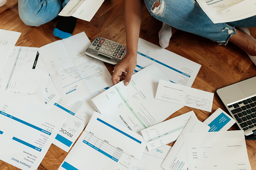 Cropped Image of Mother and Son Sitting on the Floor at Home Checking Unpaid Bills, Taxes, Due Debt, Bank Account Balance. Mom Going Through Bills With Her Son. Single Mother Managing the Debt. Bills Are All Over the Floor