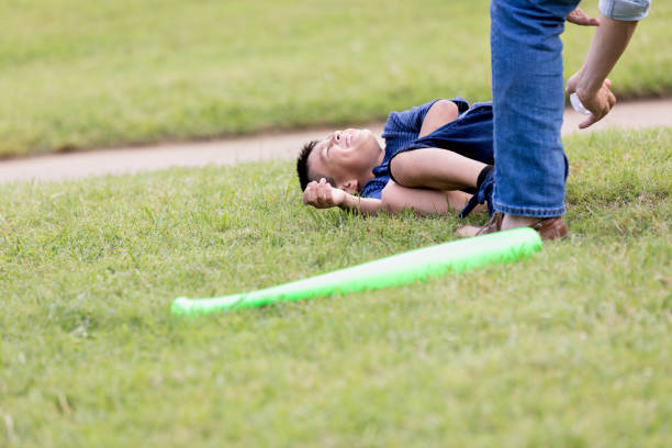 The young boy falls to the grass as the unrecognizable dad reaches down to tag him with the baseball.