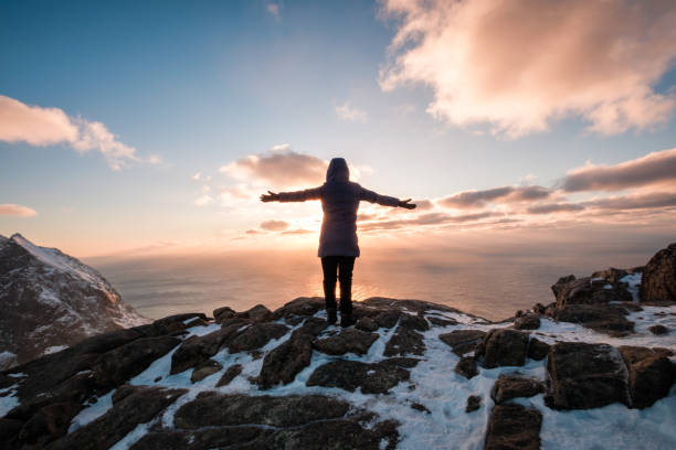 mujer escalando con la mano levantada en la montaña al atardecer - lofoten and vesteral islands beach nature norway fotografías e imágenes de stock