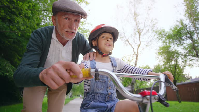 Slow motion wide shot of grandfather teaching his grandson to ride a bike and jumping from excitement in the background when the boy succeeds. Shot in Slovenia.