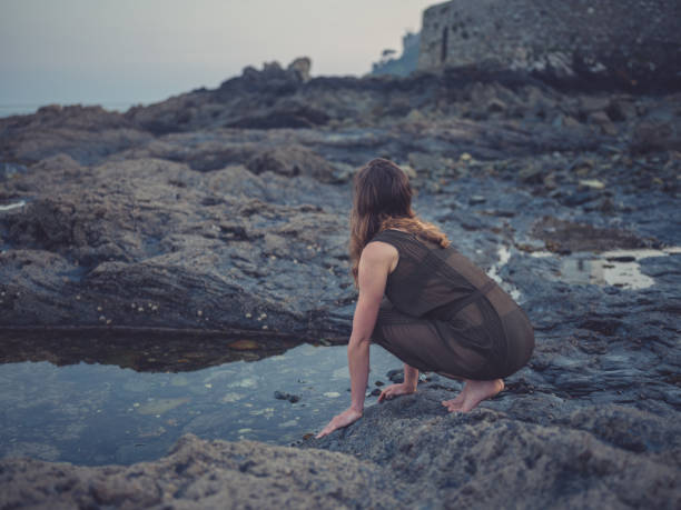 istock Young woman by rock pool on coast at sunset 1170340297