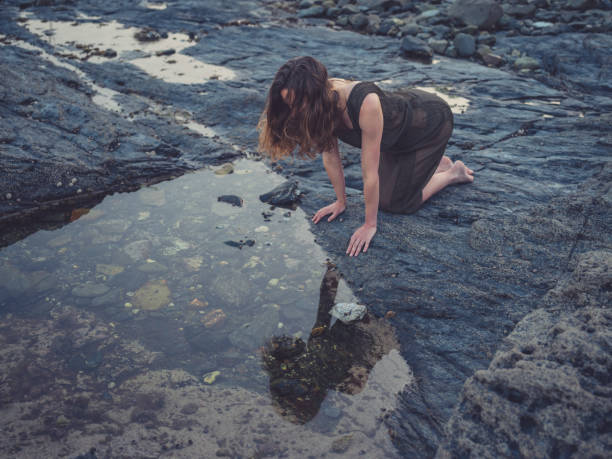 istock Young woman by rock pool on coast at sunset 1170340594