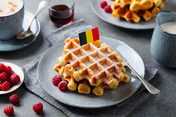 gofres con azúcar glas y bandera de bélgica en un plato. fondo gris. - waffle belgian waffle breakfast fruit fotografías e imágenes de stock