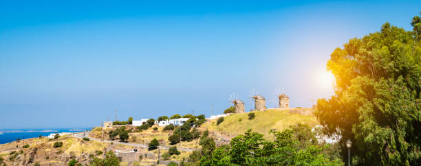 夏の日に青空の背景に対して丘の上に3つの風車と日没時のパトモス島のパノラマ風景。 - town village hill panoramic ストックフォトと画像