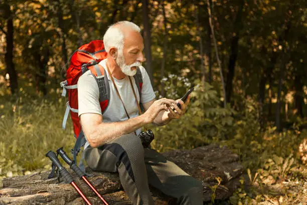 Photo of Tired Senior man resting after hiking using smart phone