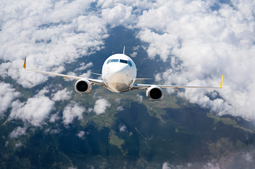 Airplane is flying over mountains in clouds. Landscape with passenger airplane, black sea mountains in low clouds, blue sky. White aircraft. Airplane climbing. Commercial plane. Aerial view. Passenger jet airplane flying above clouds