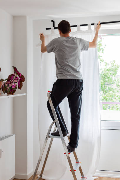 istock Man hangs white curtains on the curtain rod 1170359386
