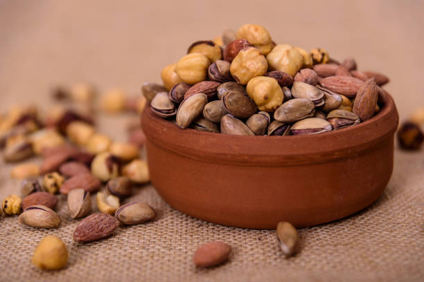 istock Almonds, pistachios, hazelnuts and round nuts in bowl on textured light brown background. Table view food. 1170359422