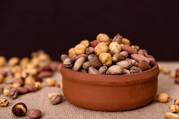 istock Almonds, pistachios, hazelnuts and round nuts in bowl on textured brown and light background. Table view food. 1170359424