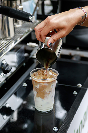 Barista preparing iced coffee. Pouring coffee into the glass with milk and ice.