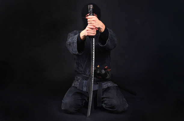 istock Ninja samurai warrior sits on his knees and covers his face with a sword. Anonymity and confidentiality concept. 1170361877