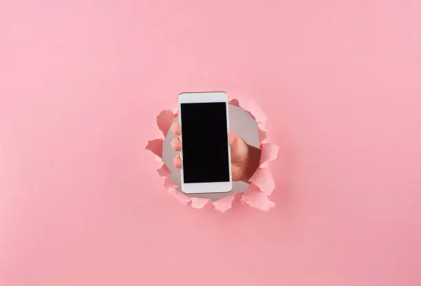 Photo of Female holding smartphone in wrapped hole in pink background, copy space