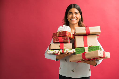 Attractive young female brunette with Christmas gifts against plain background