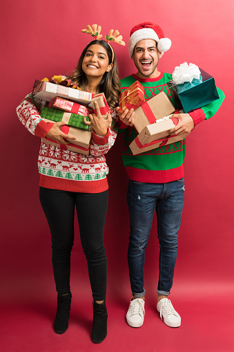 Full length of happy boyfriend and girlfriend holding gifts isolated in studio