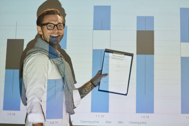 istock Cheerful excited young man in glasses holding clipboard and commenting graph on projection screen 1170370877