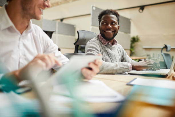 istock Positive creative multi-ethnic business specialists sitting at table in office and discussing ideas while working with internet platforms 1170370888