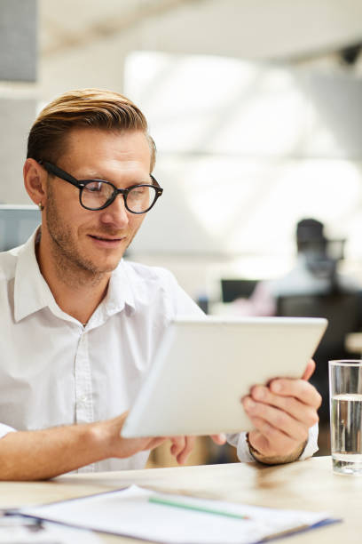istock Content clever young businessman in eyeglasses sitting at table and using tablet browsing internet 1170371142