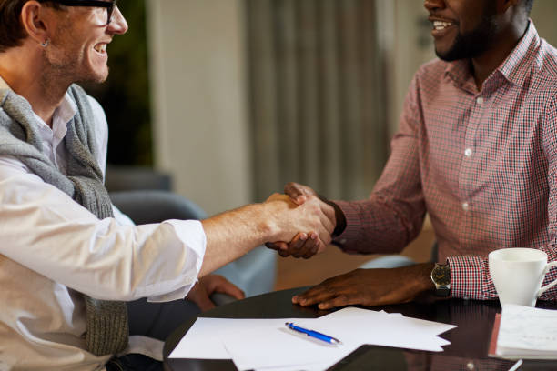 istock Close-up of excited multi-ethnic entrepreneurs sitting at table and making handshake while concluding deal after discussion of project implementation 1170371153