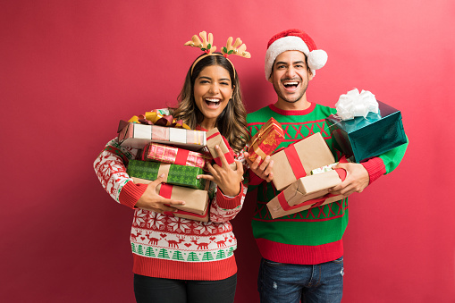 Portrait of cheerful attractive couple holding Christmas presents against plain background