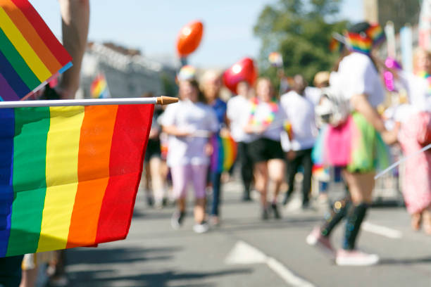 Gay Pride Parade - UK Participants and supporters of a Gay Pride Parade in Cardiff. Selective focus on a rainbow flag with unidentifiable people marching. gay pride parade photos stock pictures, royalty-free photos & images
