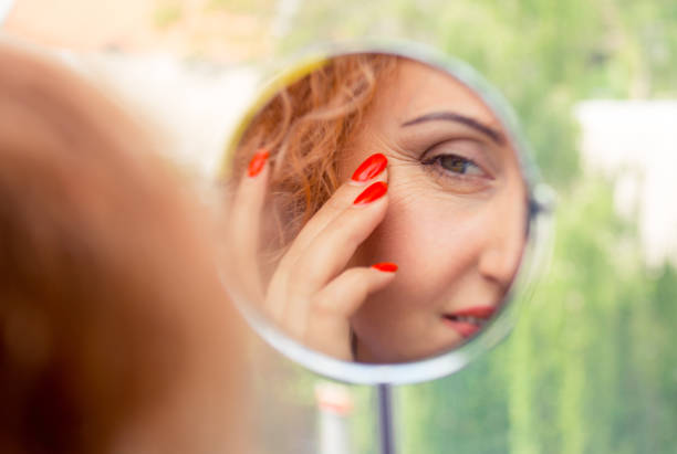 woman looks in the mirror noticing the first wrinkles stock photo