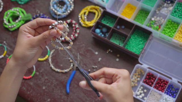 Female hands making handmade jewelry with little balls and stones
