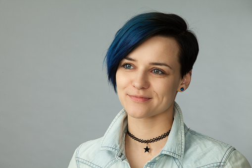 Studio portrait of an attractive 30 year old woman with blue hair in a jeans shirt on a gray background