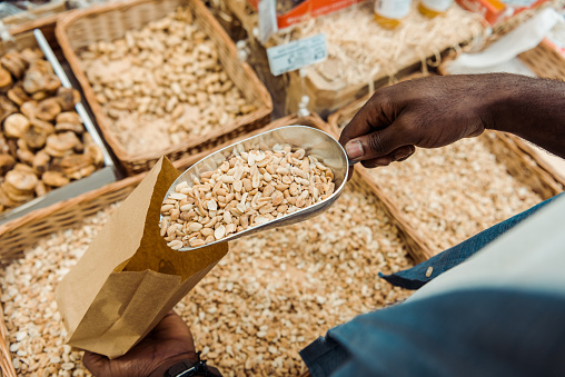 overhead view of african american man holding metal scoop with tasty peanuts in store