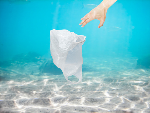 Man hand collecting plastic bag of the ocean with copy space