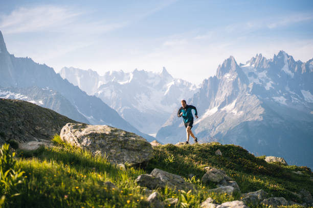 นักวิ่งเทรลวิ่งไปตามทุ่งหญ้าบนภูเขาในตอนเช้า - cross country running ภาพสต็อก ภาพถ่ายและรูปภาพปลอดค่าลิขสิทธิ์