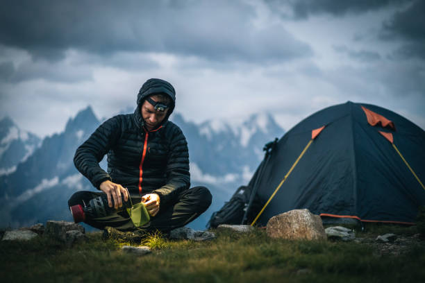 Hiker prepares hot beverage with headlamp in alpine campsite He is in an alpine meadow auvergne rhône alpes stock pictures, royalty-free photos & images