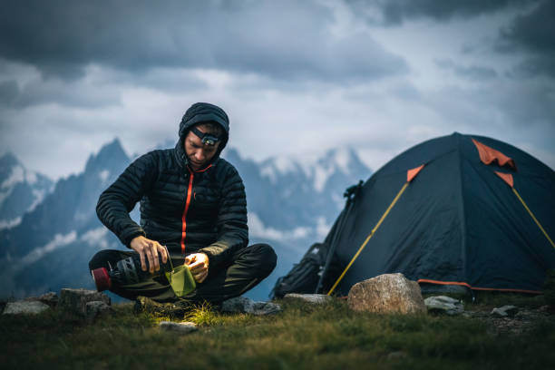 hiker prepares hot beverage with headlamp in alpine campsite - france european alps landscape meadow imagens e fotografias de stock