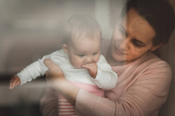 istock Affectionate mother holding her baby to look through the window 1170400179