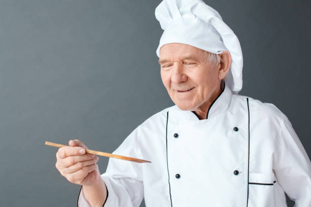 istock Senior chef studio standing isolated on gray tasting dish with spatula smiling joyful close-up 1170400556
